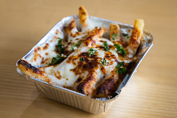 a metal take out container with baked Greek french fries loaded with melted mozzarella cheese, Greek seasoning, feta cheese, and parsley