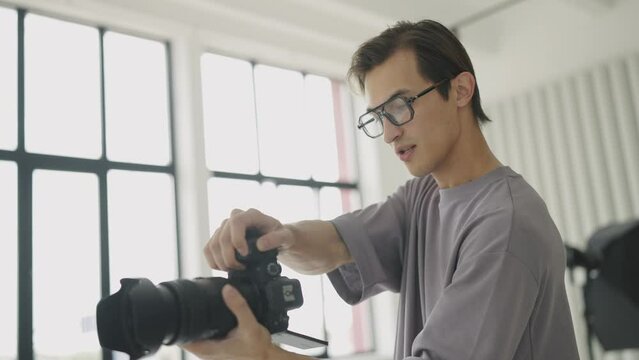 Young male photographer with glasses takes pictures with professional camera in studio. Backstage. Slow motion