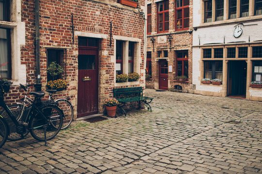 old european brick building edifice with dark red door a green bench and bicycles with windows and a green bench around a corner on a city street