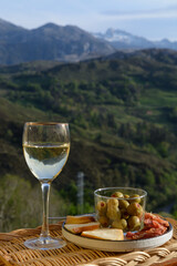 Glasses of dry white wine and spanish tapas olives in bowl with mountains peaks on background in...