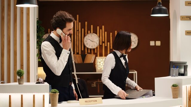 Teamworking professional hotel personnel checking tourists reservation date at check in reception desk. Receptionists coworkers discussing incoming guests booking informations
