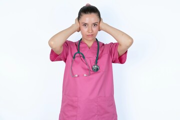 Frustrated young caucasian doctor woman wearing pink uniform over white background plugging ears with hands does not wanting to listen hard rock, noise or loud music.