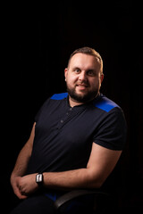 Portrait of a smiling young man with a beard. Dark background. Looks into the camera. Good-natured, contented, happy face.