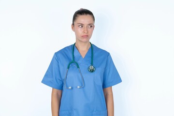 Dissatisfied young caucasian doctor woman wearing medical uniform over white background purses lips and has unhappy expression looks away stands offended. Depressed frustrated model.