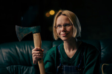 Woman smiling with an ax in her hands at home. A strong-willed woman with a strong character in glasses.