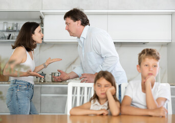 Fototapeta premium Brother and sister sitting at table in kitchen during conflict between their parents
