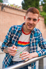 Attractive gay man painting his nails makeup with rainbow lgbt flag in the city, pride party and...