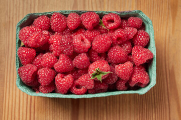 delicious fresh raw red raspberries in natural eco-friendly packaging in a green cardboard basket on a wooden table close-up. harvest. healthy food. diet. summer. vitamins