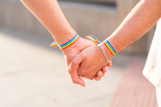 Detail of the holding hands of a couple of homosexual men with the rainbow flag at the pride party in the city, lgbt concept