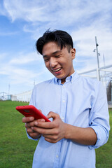 Vertical happy Asian boy using smart phone and smiling with positive attitude. Cheerful Chinese...