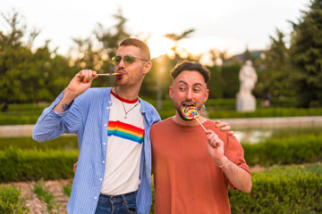 Portrait of laughing wedding couple eating a lollipop in the park on sunset in the city. Diversity and lgbt concept