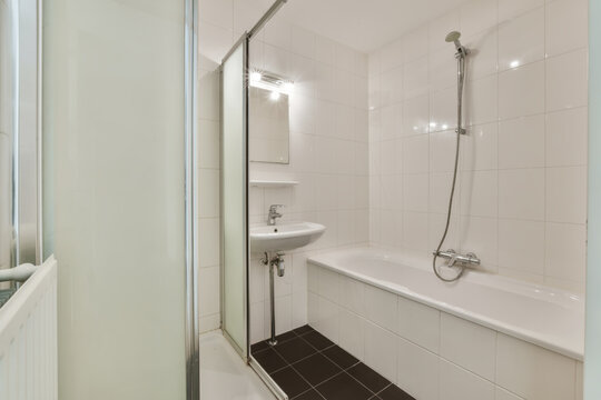 a white bathroom with black tile flooring and wall to wall glass shower stall door in the bathtub is next to the sink