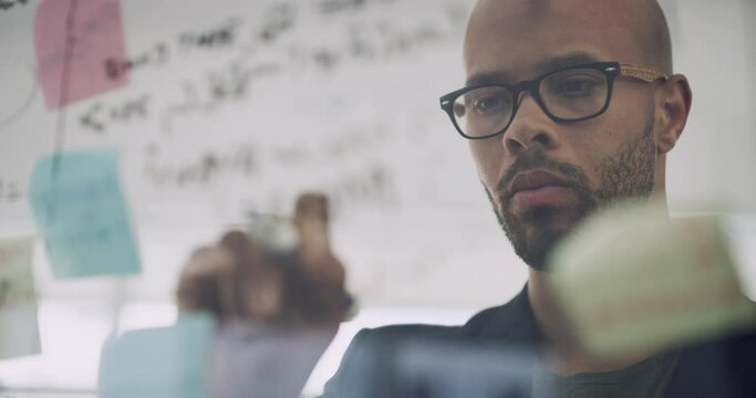 Serious businessman, writing and schedule planning with sticky note for brainstorming, ideas or strategy at office. Thoughtful man employee thinking in project plan, task or taking notes at workplace
