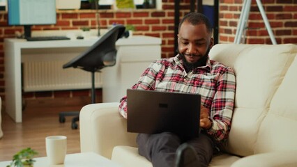 Easy going african american employee working from home on laptop, Teleworker remotely doing various tasks, typing on keyboard in stylish cozy warm apartment personal office