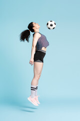 Successful female athletic woman, soccer player, jumping high up playing soccer ball
