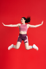 Fototapeta na wymiar Sporty athletic woman doing gym exercises, jumping high, isolated on red background