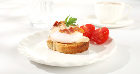 toast with poached egg and bacon on a plate. serving breakfast on a white plate with tomato. sunny day. angle view. 