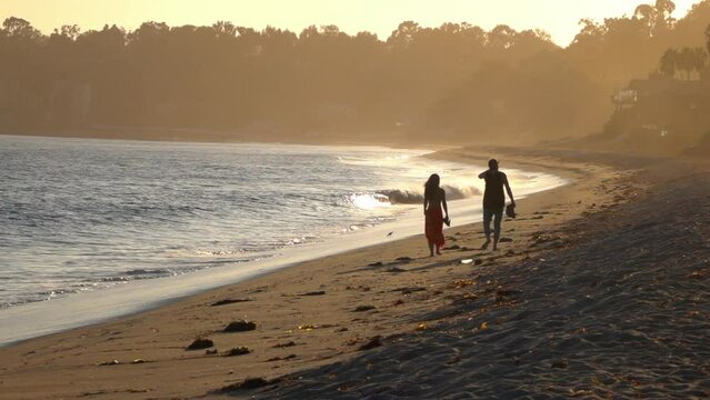 Lockdown Slow Motion Shot Of Couple Walking Together On Shore By Waves At Beach During Sunset - Napa Valley, California