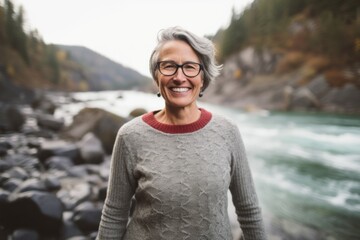 Fototapeta na wymiar Medium shot portrait photography of a grinning woman in her 50s that is wearing a cozy sweater against a river or waterfall background . Generative AI