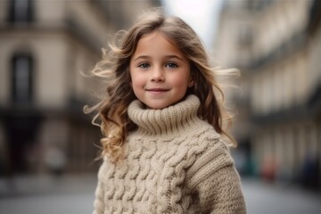 Fototapeta premium Portrait of a beautiful little girl in a warm knitted sweater on the street.