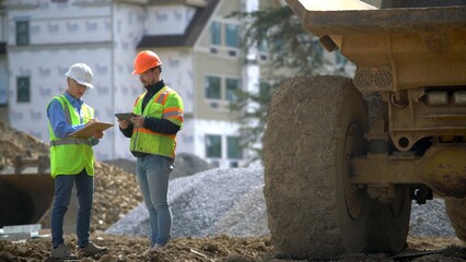Construction site foreman talks with woman project engineer next to a dump truck in front of building. © Robert Peak
