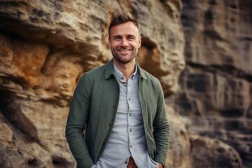 Portrait of a handsome young man standing with hands in pockets against rock background