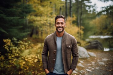 Handsome man standing in autumn forest. Smiling and looking at camera.