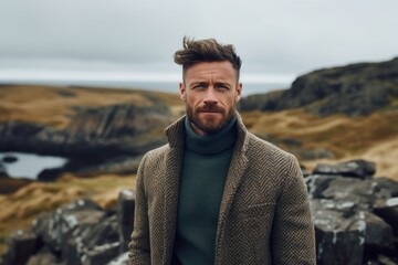 Fototapeta na wymiar Portrait of a handsome bearded man in a coat and sweater standing in a field on the Isle of Skye, Scotland