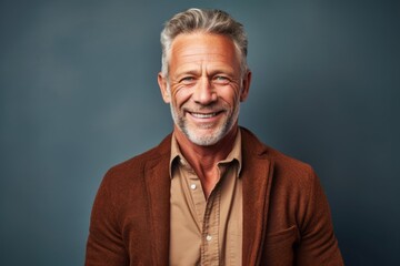 Obraz premium Portrait of a handsome senior man smiling at the camera while standing against grey background