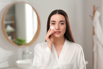 Beautiful woman removing makeup with cotton pad indoors