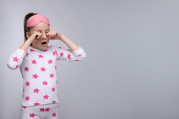 Girl with sleep mask yawning on light grey background, space for text. Insomnia problem