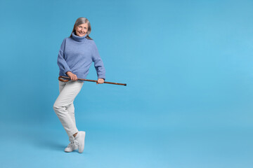 Senior woman with walking cane on light blue background, space for text