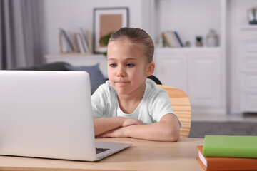 Little girl using laptop at table indoors. Internet addiction
