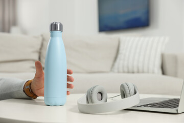 Man taking thermo bottle from white table at home, closeup