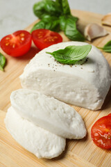 Delicious mozzarella with tomatoes and basil leaves on wooden board, closeup