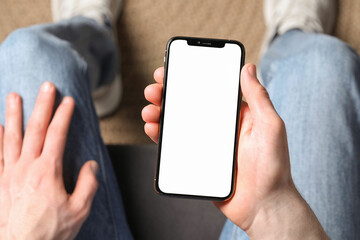 Man holding smartphone with blank screen indoors, top view. Mockup for design