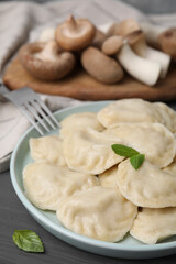 Fototapeta na wymiar Plate of delicious dumplings (varenyky) with mushrooms served on grey wooden table, closeup