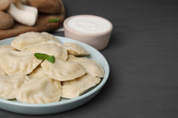 Fototapeta na wymiar Plate of delicious dumplings (varenyky) with mushrooms on grey wooden table, closeup. Space for text
