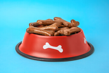 Red bowl with bone shaped dog cookies on light blue background, closeup