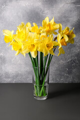 Bouquet of beautiful yellow daffodils in vase on grey wooden table