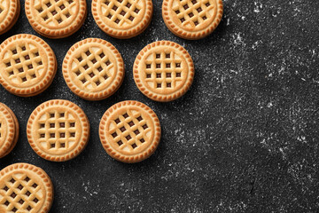 Tasty sandwich cookies with cream on black textured background, flat lay. Space for text
