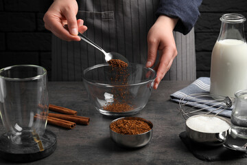 Making dalgona coffee. Woman pouring instant granules into bowl at grey table, closeup