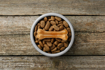 Dry dog food and treat (chew bone) on wooden floor, top view