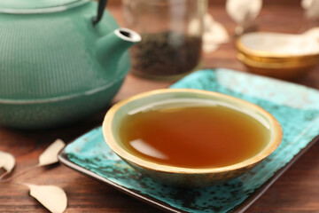 Teapot and cup of freshly brewed tea on wooden table, closeup. Traditional ceremony