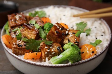 Bowl of rice with fried tofu, broccoli and carrots on table, closeup