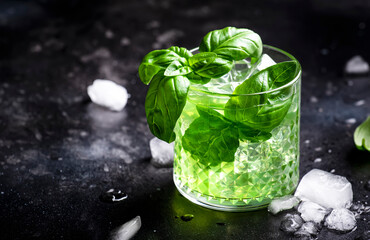 Basil smash alcoholic cocktail drink with dry gin, syrup, lemon, basil and ice, dark bar counter background