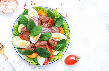 Perigord salad with roasted chicken liver, red tomatoes, cucumbers, boiled eggs, lettuce and spinach. Black kitchen table background, top view