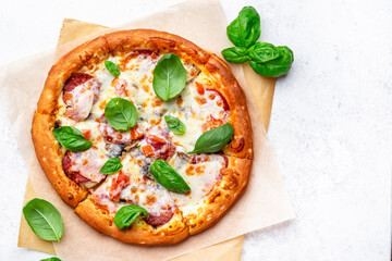 Pizza with spicy salami sausage, mozzarella cheese, tomato sauce and green basil, gray table background, top view