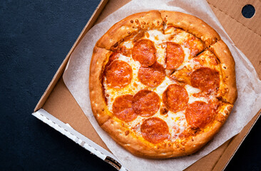 Pepperoni pizza in box with spicy salami sausage, mozzarella cheese, tomato sauce, just delivered,, black table background, top view