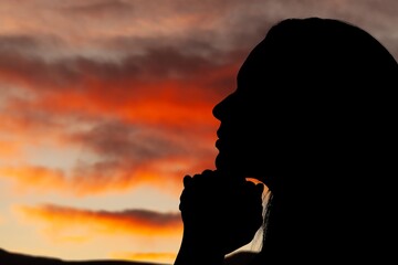 Silhouette of young woman praying to God on sky background.